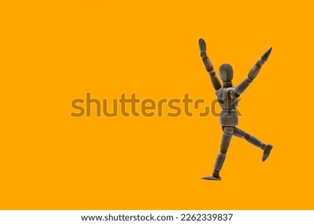 Photograph of a dark colored wooden mannequin with orange background, it is in motion, with arms open and stretched upwards. Photo to be able to cut out. Concepts. Selective focus. Space for copy