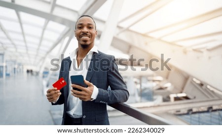 Portrait Of Smiling Black Man With Smartphone And Credit Card In Hands Standing At Airport Terminal, Happy African American Businessman In Suit Making Online Shopping Or Money Transfers, Panorama