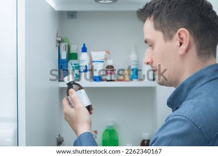 Man hold medication bottle reading instruction or prescription on packaging. Man looking at bottles from medicine cabinet Royalty-Free Stock Photo #2262340167