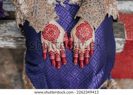 Close up shot of beautiful hands of a bride with red henna wedding design. Bride with purple dress.