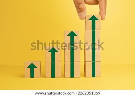 Business growth success process,increasing business concept.Hand Putting Wooden cubes on stacked with Arrow Up icon over yellow background suitable for business,finance,background idea.