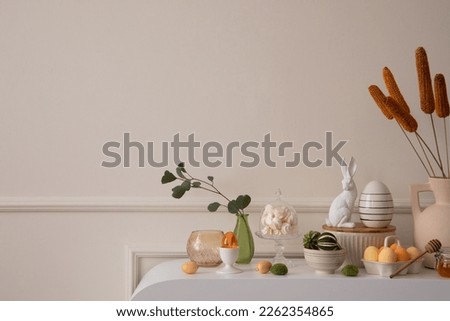 Minimalist composition of easter living room interior with copy space, easter bunny sculpture, colorful easter eggs, vase with leaves, wall with stucco and personal accessories. Home decor. Template. Royalty-Free Stock Photo #2262354865