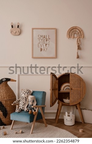 Minimalist composition of kid room interior with mock up poster frame blue armchair, plush toys, wooden blocks, rattan sideboard, beige wall with stucco, braided penguin and accessories. Home decor. 