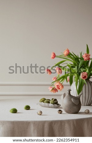 Minimalist composition of easter dining room interior with copy space, vase with tulips, colorful eggs, gray hen sculpture, beige wall with stucco and personal accessories. Home decor. Template. 