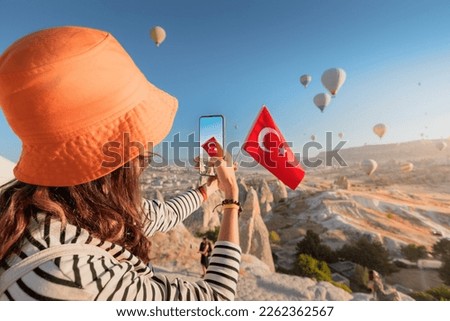 a travel blogger girl takes photos of flying balloons in Cappadocia and the Turkish flag. Social media influencer