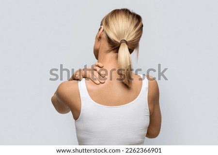 Rear view of tired blonde woman in white top rubbing neck, suffering from office syndrome after working day, isolated on grey studio background, copy space. Back pain, osteochondrosis concept Royalty-Free Stock Photo #2262366901
