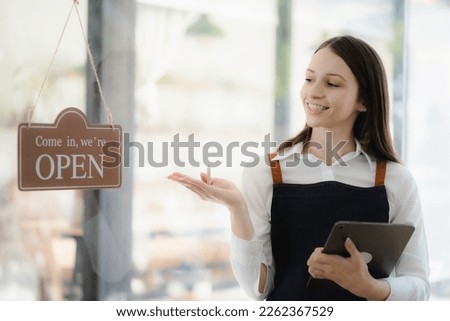 Startup, successful small business owner standing with tablet with open sign in front of coffee shop. Portrait of female barista owner. SME business seller concept.
