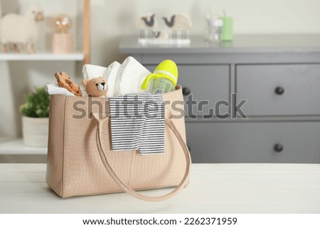 Mother's bag with baby's stuff on white wooden table indoors. Space for text Royalty-Free Stock Photo #2262371959