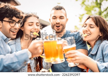 Young people drinking and toasting beer pints at brewery bar garden out doors - Food and beverage life style concept with guy and girls having fun together at happy hour - Bright vivid sunny filter