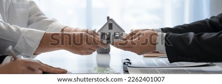 Young Asian real estate agent, and insurance salesman handing over a sample house to a client after signing the sale at the office.

