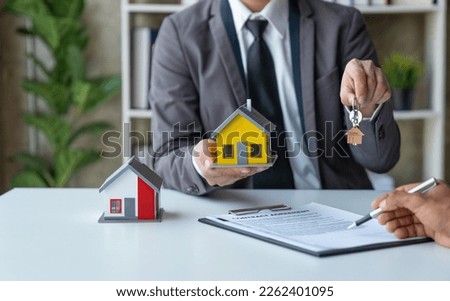 Young Asian real estate agent, and insurance salesman handing over a sample house to a client after signing the sale at the office.