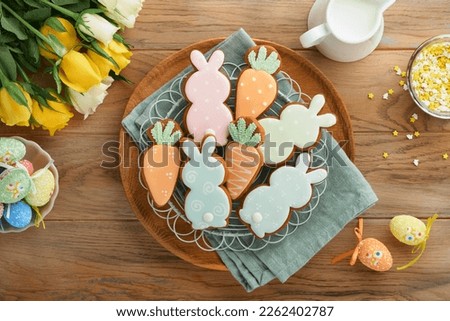 Easter breakfast Holliday concept. Easter gingerbread shape of bunny and carrot with cinnamon with colored glaze, easter decorations, colored eggs on old wooden background. Easter Holliday card.  Royalty-Free Stock Photo #2262402787
