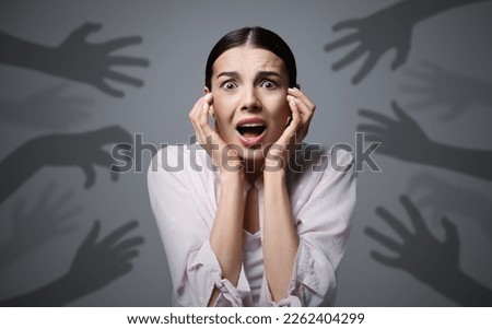 Paranoid delusion. Scared woman screaming on grey background. Shadows of hands reaching for her symbolizing fear and anxiety Royalty-Free Stock Photo #2262404299