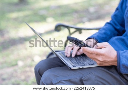 Man using smartphone and laptop working in the park.