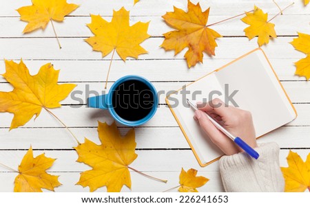 Female hand writing something in notebook near cup of coffee.