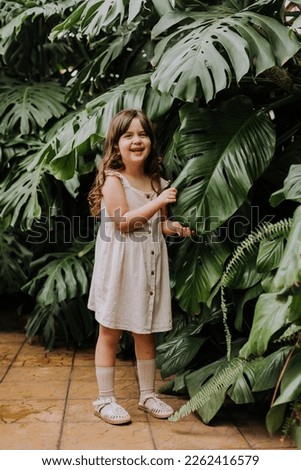 The face of a little girl surrounded by tropical leaves. Portrait of a beautiful baby with perfect skin and dark hair close-up. Natural cosmetics, health, cleanliness, skin care, beauty concept. 