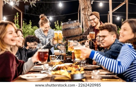 Young men and women having fun drinking out at beer garden patio - Social gathering and beverage life style concept on happy people enjoying weekend cookout time together at night - Vivid dark filter Royalty-Free Stock Photo #2262420985