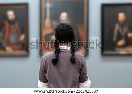 Back view of young woman contemplates ancient pictures. Student visiting arts exhibition. Museum day. Concept of modern culture education.