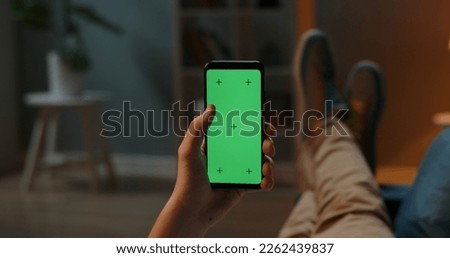 Man lying on couch using smartphone with chroma key green screen at night, scrolling through social media or online shop - internet, communications concept close up 