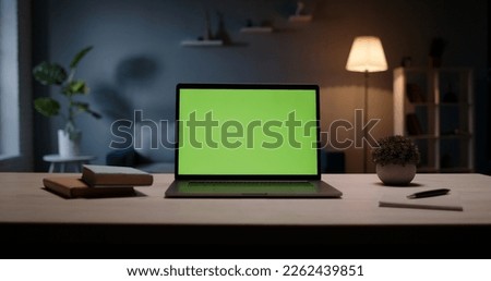 Close up shot of modern chroma key green screen laptop computer set up for work on desk at night - remote work, technology concept