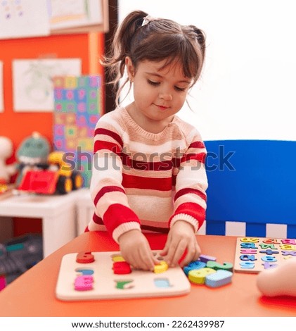 Adorable hispanic girl playing with maths puzzle game standing at kindergarten Royalty-Free Stock Photo #2262439987