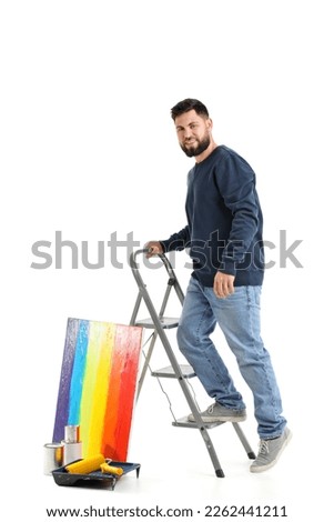 Young man with ladder and painting on white background
