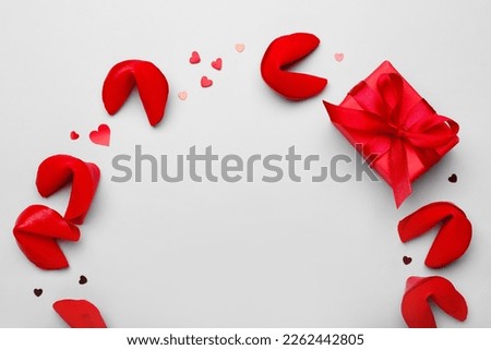 Frame made of red fortune cookies with gift and hearts on grey background. Valentine's Day celebration