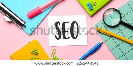 Paper sheet with abbreviation SEO and stationery on pink background