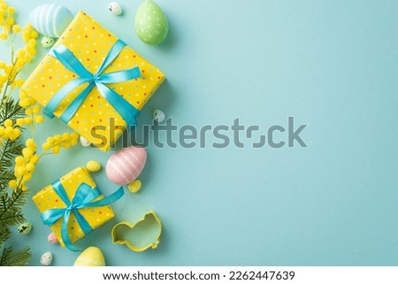 Easter celebration concept. Top view photo of yellow present boxes with blue ribbon bows colorful easter eggs mimosa flowers and baking mold on isolated pastel blue background with empty space