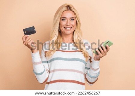 Photo of cheerful satisfied woman with curly hairstyle striped long sleeve hold phone debit card isolated on pastel color background