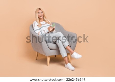 Full length size photo of young positive woman dreamy look excited with phone empty space chair wear casual shirt isolated on beige color background