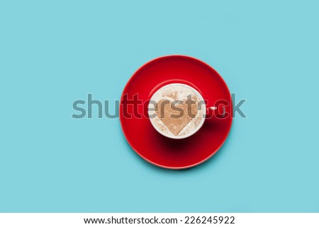 Cup of coffee with heart shape symbol on color background.