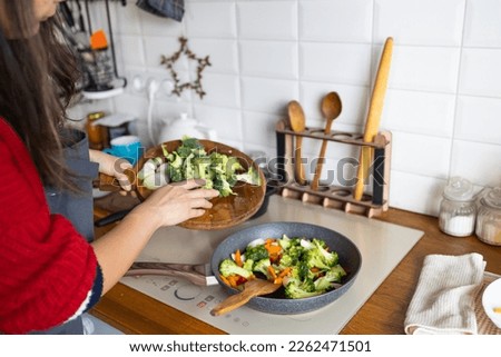 Woman cooking frying fresh healthy vegetables on pan on induction stove. Lifestyle background.  Royalty-Free Stock Photo #2262471501