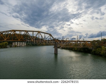 a long rusty railroad bridge over the green waters of the Tennessee River surrounded by autumn colored trees and lush green trees with powerful clouds at sunset in Knoxville Tennessee USA