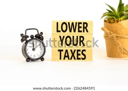 Lower your taxes symbol. Concept words Lower your taxes on wooden blocks on a beautiful white table white background. Black alarm clock. House plant. Business tax lower your taxes concept. Copy space.