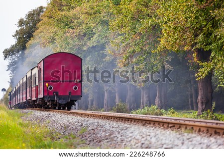 Back of a steam train with a red rail car at the end on a track through beautiful landscape/Railroad Farewell View Royalty-Free Stock Photo #226248766