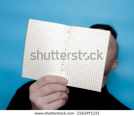Blank notepad in a cage for text in the hands of a young man in black golf on a blue background. Notes copy space. Place for text banner notepad. Write a message in notepad