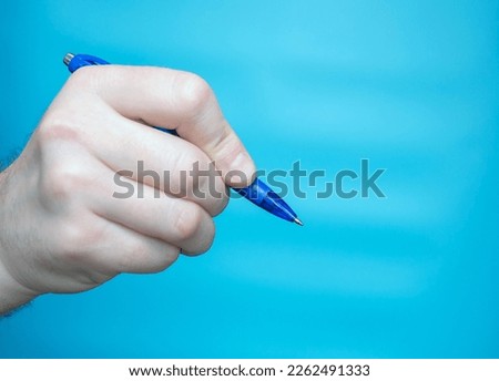 Business concept hand of man with blue pen. Close-up Studio shot of a man holding a pen with his fingers for writing on a blue background. Writing letter or text copy space