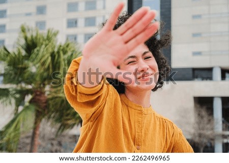 Front view of a shy latin girl hiding from the camera. Happy hispanic young woman smiling and covering her face with her hand palm. High quality photo Royalty-Free Stock Photo #2262496965