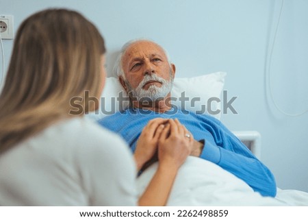 Rear view of woman caressing ill man in hospital room. Shot of a woman visiting an elderly patient in a hospital. In the Hospital Ward Recovering Father is Visited by Daughter. Senior Sick Man Royalty-Free Stock Photo #2262498859