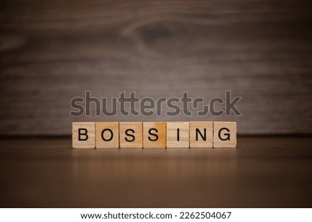 The word bossing composed of wooden cubes tablets on a dark wooden background