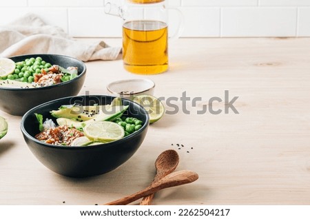 Buddha bowl with crispy sesame chicken. Sweet and sour fried chicken with steamed rice, peas and acocado on light wooden background. Healthy and balanced food concept. Selective focus with copy space Royalty-Free Stock Photo #2262504217