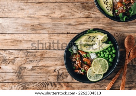 Buddha bowl with crispy sesame chicken asian style. Sweet and sour fried chicken with steamed rice, peas and acocado on rustic background. Healthy and balanced food concept. Top view with copy space Royalty-Free Stock Photo #2262504313