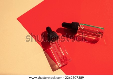 Two glass bottles with cosmetic liquid on bright red background with shadows and light reflections. Flat lay style and close-up. Copy space for your design