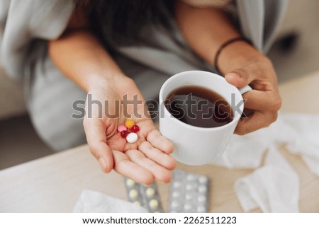 A woman with a cold with pills is treated at home chooses which drugs to take and self-medicates, checks the expiration date while sitting on the couch at home Royalty-Free Stock Photo #2262511223