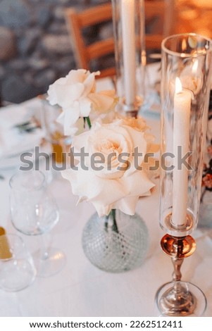The decor of the wedding dinner in the restaurant. Round tables are decorated with fresh flowers, white roses and candles. Wedding banquet in white colors Royalty-Free Stock Photo #2262512411