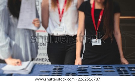 Process of checking in on a conference congress forum event, registration desk table, visitors and attendees receiving a name badge and entrance wristband bracelet and register electronic ticket
 Royalty-Free Stock Photo #2262516787