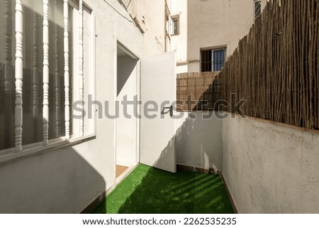 Small terrace of a house on the ground floor with artificial grass floor and reeds to hide from view