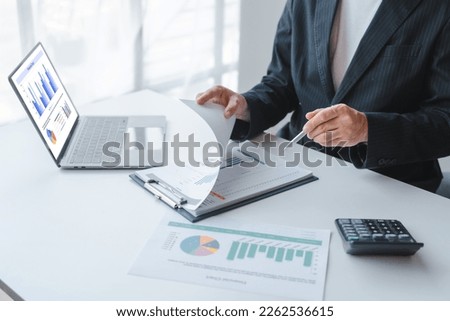 Young handsome asia business man in formal suit working with monthly report balance sheet and yearly tax of accounting to verify the account by an authorized auditor