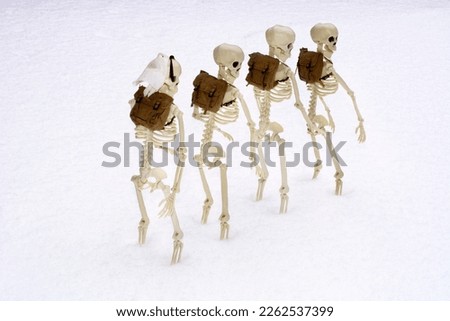 Line of skeletons carrying brown backpacks climbing up snow covered mountain in winter
